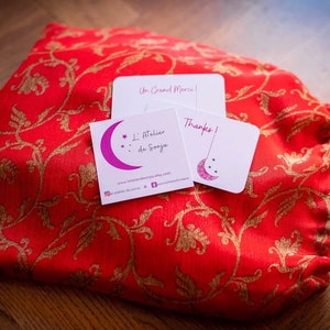 May include: A red fabric pouch with gold floral embroidery and a white card with the text "Un Grand Merci!" and a white card with the text "Thanks!" and a business card with the text "L'Atelier de Sonja" and a website address.