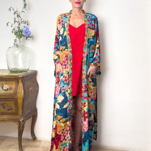 May include: A long, flowing floral print robe with a red slip dress underneath. The robe has a deep V-neckline and long sleeves. The floral print is in shades of blue, yellow, red, and green.