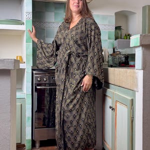 May include: A woman wearing a long, black and gold patterned robe with a V-neck and long sleeves. The robe has a belt and a geometric pattern.