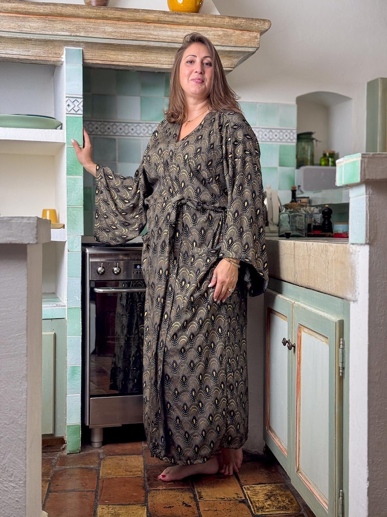 May include: A woman wearing a long, black and gold patterned robe with a V-neck and long sleeves. The robe has a belt and a geometric pattern.