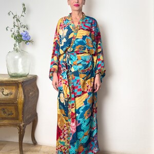 May include: A long, colourful robe with a floral print in shades of blue, yellow, red, and pink. The robe has a wide, flowing sleeve and a sash that ties at the waist.