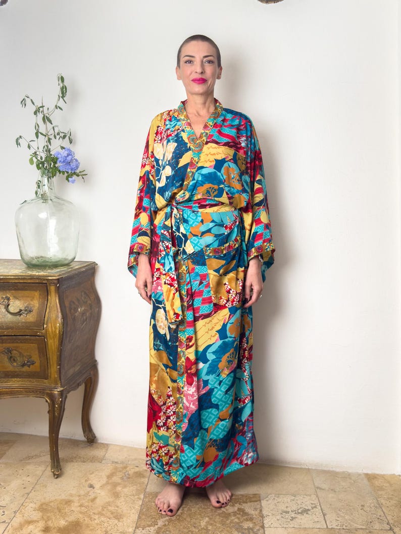 May include: A long, colourful robe with a floral print in shades of blue, yellow, red, and pink. The robe has a wide, flowing sleeve and a sash that ties at the waist.