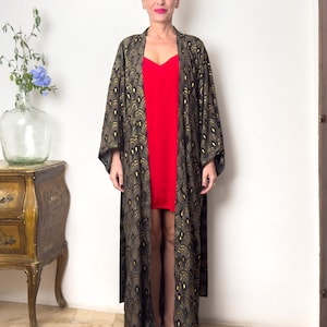 May include: A long black and gold kimono with a peacock feather pattern. The kimono is worn over a red slip dress.