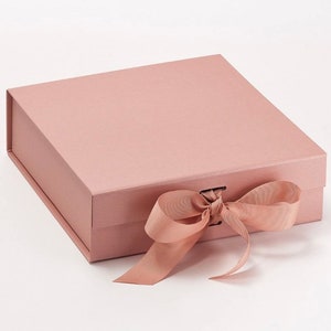 May include: A blush pink gift box with a satin ribbon tied in a bow. The box is made of sturdy cardboard and has a magnetic closure.