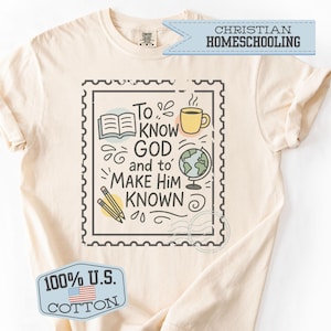 May include: Cream-colored t-shirt with a graphic featuring the text "To Know God and to Make Him Known" inside a postage stamp design. The design includes a book, coffee cup, globe, and pencils. The shirt also has a "100% U.S. Cotton" tag.