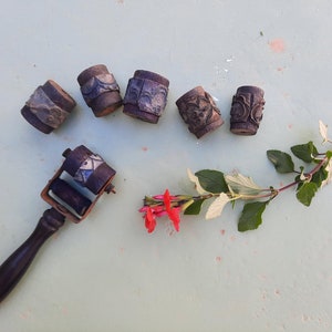 Peut inclure: Six blocs d'impression en bois vintage avec des motifs complexes, et un rouleau en bois avec une poignée, le tout sur une surface vert clair avec une brindille de fleurs rouges.