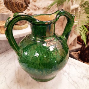 Peut inclure: Pichet en céramique verte fait à la main avec une finition brillante. Le pichet présente un corps arrondi, un large bec et une anse incurvée. L'intérieur est de couleur beige clair. Le pichet est probablement vintage ou antique.