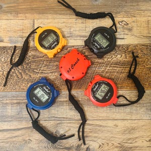 May include: Five digital stopwatches with black lanyards. The stopwatches are yellow, red, black, blue, and red with the text "#1 Coach".