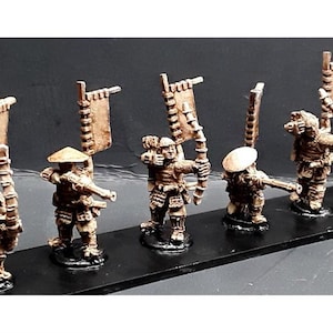 Puede incluir: Un conjunto de siete figuras en miniatura de guerreros japoneses, cada uno con una lanza y una bandera. Las figuras están pintadas en tonos marrones y blancos, y están de pie sobre una base negra.