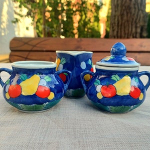 May include: A blue and white ceramic tea set with a pitcher, sugar bowl, and creamer. The set is decorated with a fruit motif, including pears, apples, and lemons.