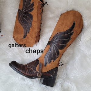 May include: A pair of brown leather chaps with a wing design. The chaps are made of suede and have a buckle closure. The word "gaiters" and "chaps" are written on the white surface below the chaps.