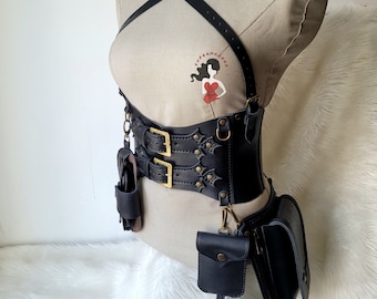 May include: Black leather harness with a wide belt, two buckles, and multiple pouches. The harness has a criss-cross strap design and is decorated with metal accents.