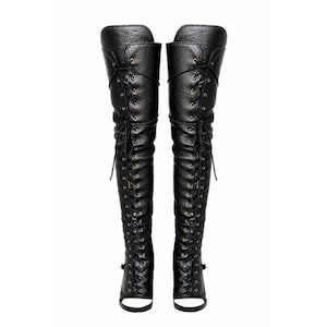 May include: A pair of black over-the-knee boots featuring a textured finish, a full-length front lace-up closure with metallic eyelets, and an open-toe design with a strap across the base of the foot, extending high up the leg in a fitted silhouette.