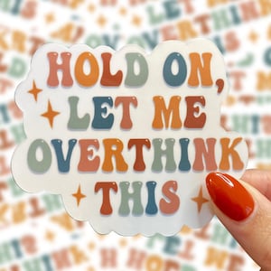 Op de afbeelding: Een sticker met de tekst "HOLD ON, LET ME OVERTHINK THIS" in retro-stijl. De sticker heeft een witte achtergrond met een wolkachtige vorm en wordt door een hand vastgehouden.