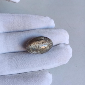 May include: A smooth, oval-shaped, grey and white gemstone with a silvery sheen.