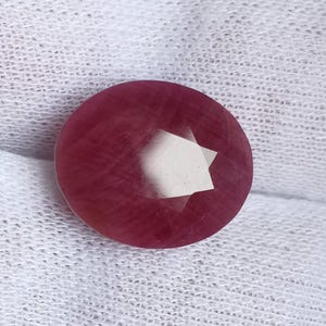 以下が含まれることがあります： 星型のカットが施された丸いファセットカットのルビーの宝石。ルビーは濃い赤色で、研磨仕上げが施されています。