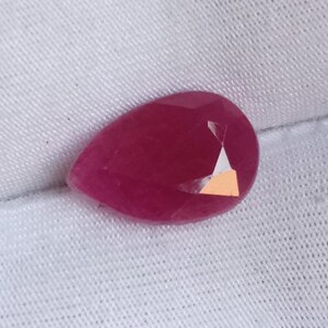 May include: A pear-shaped, deep pink gemstone with facets.