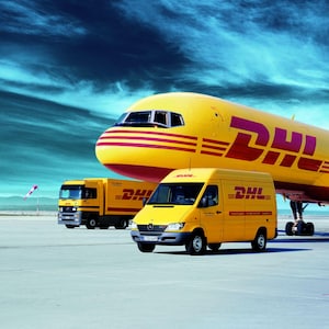 May include: A yellow DHL cargo plane parked on a tarmac next to a yellow DHL delivery truck and a smaller yellow DHL van. The plane has the DHL logo on the side and the van has the DHL logo on the side.