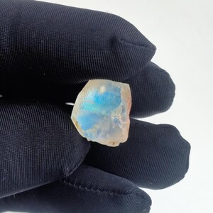 Puede incluir: Una piedra preciosa blanca, transl&uacute;cida e iridiscente con destellos azules y verdes. La piedra preciosa tiene una forma irregular y una superficie rugosa.