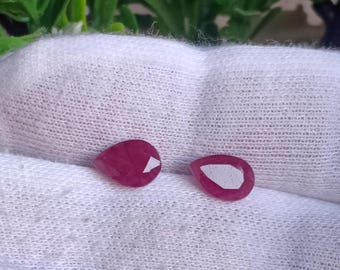 May include: Two pink pear-shaped gemstones on a white fabric background.