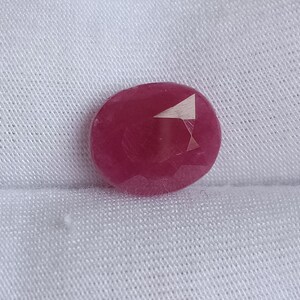 Puede incluir: Una piedra preciosa ovalada de color rosa intenso con una pequeña inclusión triangular blanca.