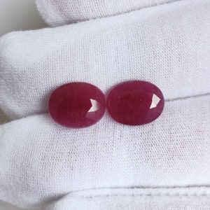 May include: Two oval-shaped, deep red gemstones. The gemstones are smooth and polished.