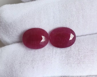 Puede incluir: Dos piedras preciosas de forma ovalada de color rojo intenso. Las piedras preciosas son lisas y pulidas.