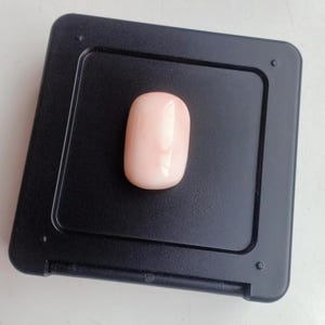 May include: A pale pink oval-shaped coral gemstone displayed on a black background.
