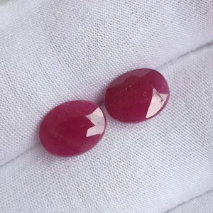 May include: Two oval-shaped, deep pink gemstones with a smooth, polished surface.