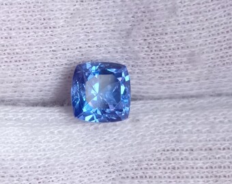 May include: A cushion-cut blue gemstone with a faceted surface.