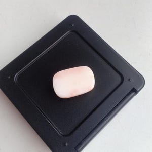 May include: A pale pink oval-shaped gemstone on a black background.