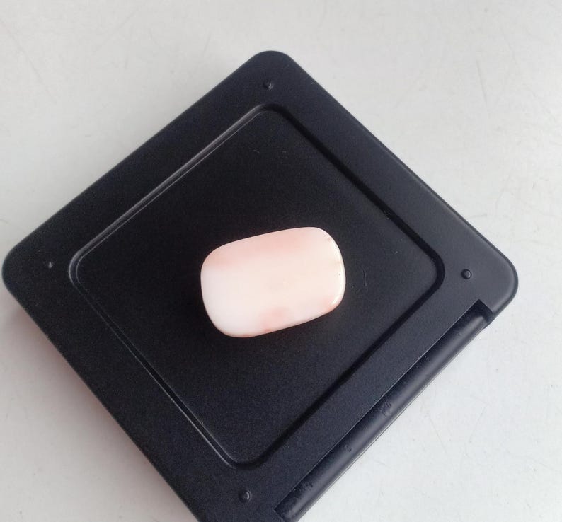 May include: A pale pink oval-shaped gemstone on a black background.