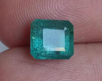 May include: A vibrant green emerald gemstone with a square cut and a slightly cloudy appearance.