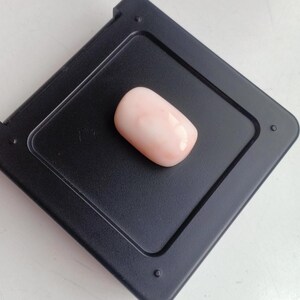 May include: A pink and white oval-shaped coral cabochon gemstone on a black background.