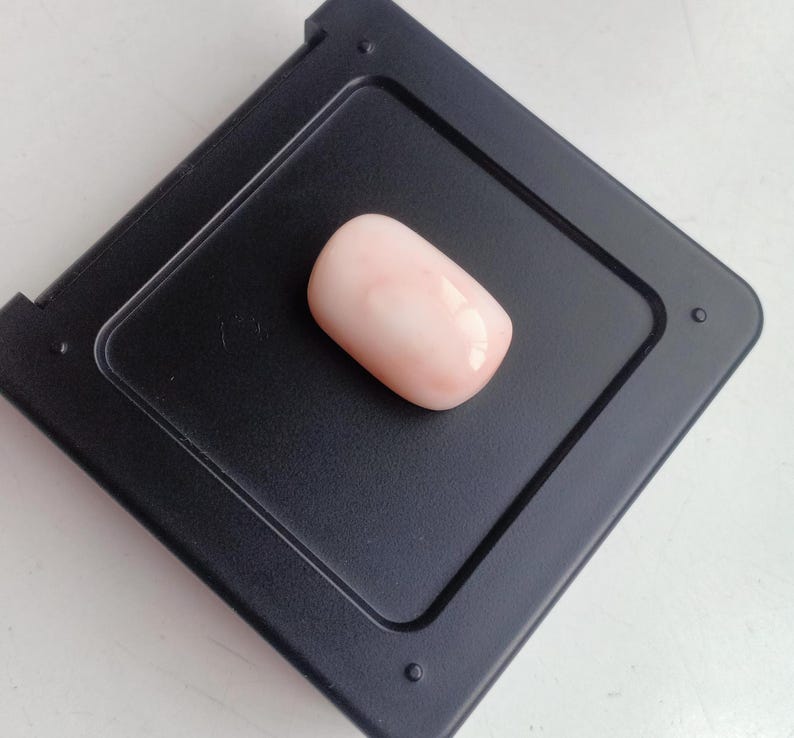 May include: A pink and white oval-shaped coral cabochon gemstone on a black background.