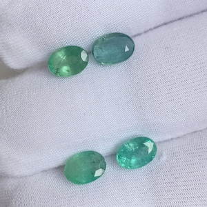 May include: Four oval-cut gemstones in shades of green and teal. The gems are displayed on a white fabric background, showcasing their facets and clarity. These gemstones are likely for jewellery making.