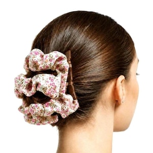 May include: A hair accessory featuring a brown plastic claw clip integrated with a gathered, ruffled fabric scrunchie. The fabric is light pink and decorated with a small-scale floral pattern in shades of pink, green, and brown.