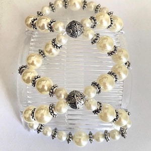 May include: Three hair combs with faux pearl beads and silver-colored accents. The combs are clear and the text "Ornate Pearl with clear combs" is at the bottom of the image. The pearls are cream-colored and the silver accents are ornate.