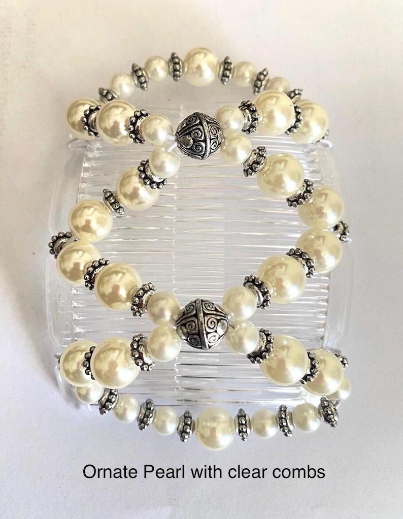 May include: Three hair combs with faux pearl beads and silver-colored accents. The combs are clear and the text "Ornate Pearl with clear combs" is at the bottom of the image. The pearls are cream-colored and the silver accents are ornate.