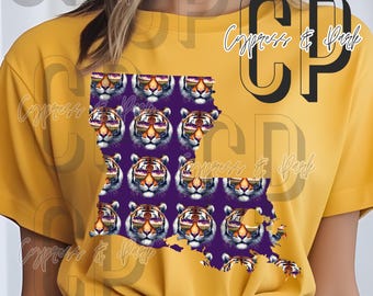 Pode incluir: Camiseta amarelo mostarda com um contorno roxo do estado da Louisiana preenchido com rostos de tigre usando óculos de sol. A camisa tem o texto "Cypress & Park" em uma fonte de script.