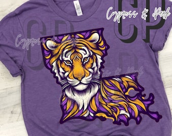 Pode incluir: Camiseta roxa com um gráfico de uma cabeça de tigre dentro do contorno do estado da Louisiana. O tigre é amarelo, laranja e branco com detalhes roxos e dourados.