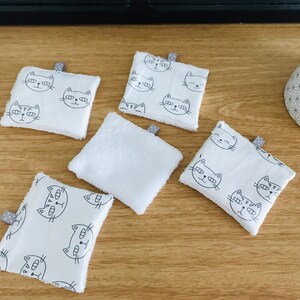 May include: Five white cotton washcloths with a black cat face design. The washcloths are square and have a gray tag attached to one corner.