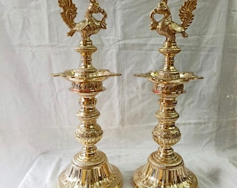 Puede incluir: Dos lámparas de aceite de metal dorado adornadas con remates en forma de pavo real. Las lámparas tienen un diseño tradicional indio con detalles intrincados y una base redonda.