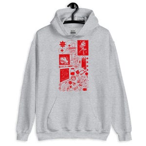 May include: A gray hoodie with a red graphic design. The design features various illustrations, including a boombox, a person, and other objects. The word "RED" is also included in the design.