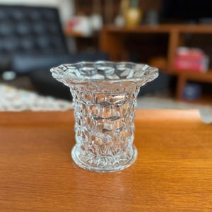 May include: A clear, vintage-style glass vase with a diamond pattern and scalloped rim. The vase is approximately 6 inches tall and sits on a wooden surface. The design is a classic, decorative piece.