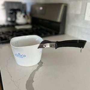 May include: White ceramic measuring cup with a blue floral design and a black and silver handle.