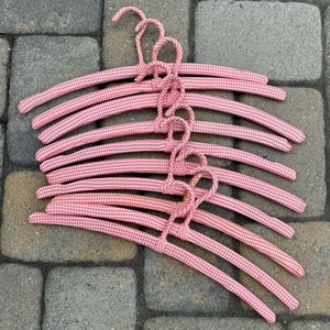 Puede incluir: Una pila de perchas de alambre con estampado de vichy rosa y blanco. Las perchas est&aacute;n todas anidadas, con el gancho de la percha superior visible.