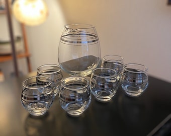 Puede incluir: Un juego de siete vasos para beber de vidrio transparente con bandas plateadas. El juego incluye una jarra y seis vasos.