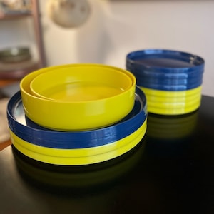 May include: A set of yellow and blue nesting bowls. The bowls are stacked on top of each other, with the yellow bowls on the bottom and the blue bowls on top.