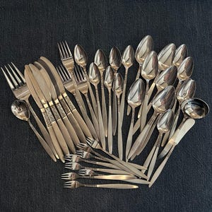 May include: A set of silverware with a floral pattern on the handles. The set includes forks, knives, spoons, and a serving spoon. The silverware is made of stainless steel and has a polished finish.